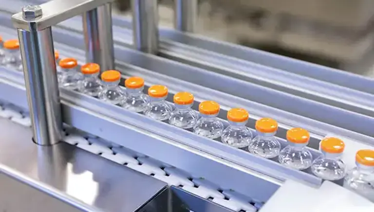 Close up of clear glass medicines bottles moving through a production line in a factory 