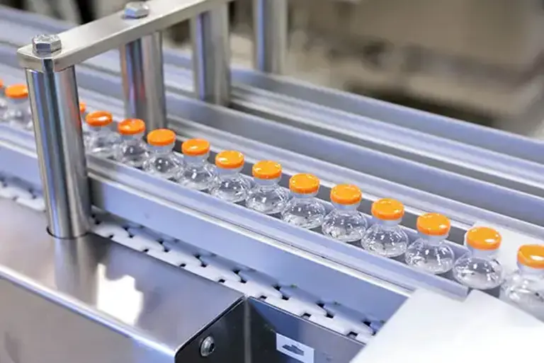 Close up of clear glass medicines bottles moving through a production line in a factory 