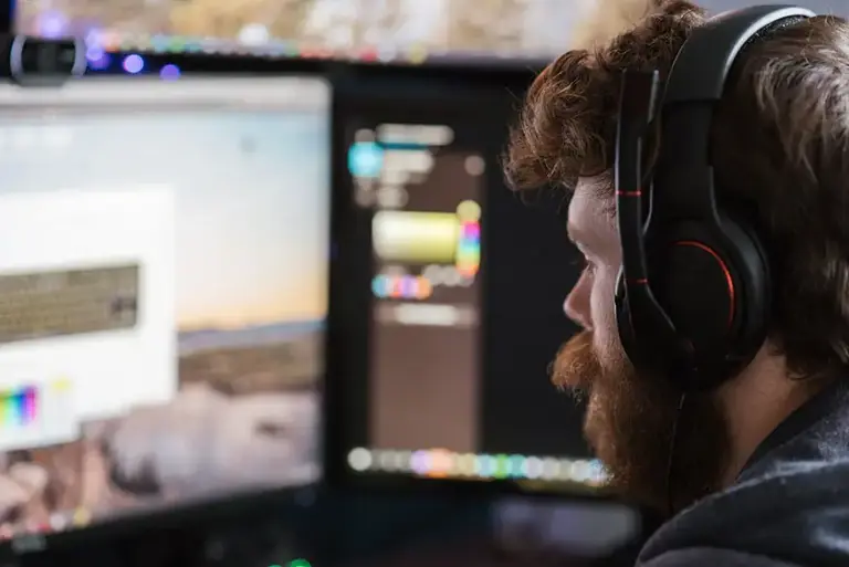 Close up of man wearing headphones is seen working on two large monitors