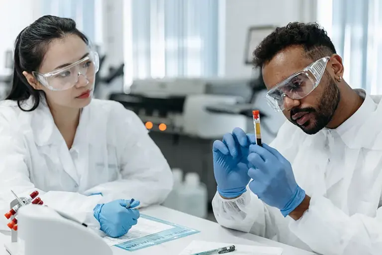 Two scientists carefully study a vial containing a blood sample.