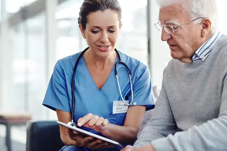 Healthcare professional sits with an older man to explain something on a clipboard