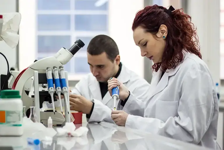 Two scientists in a lab both working with pipettes