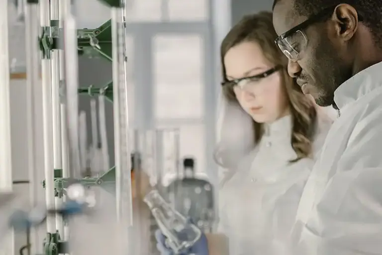 A pair of scientists stand to the side while they examine long titration tubes