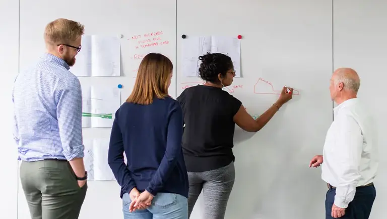 Four office workers drawing on sheets stuck on the wall 