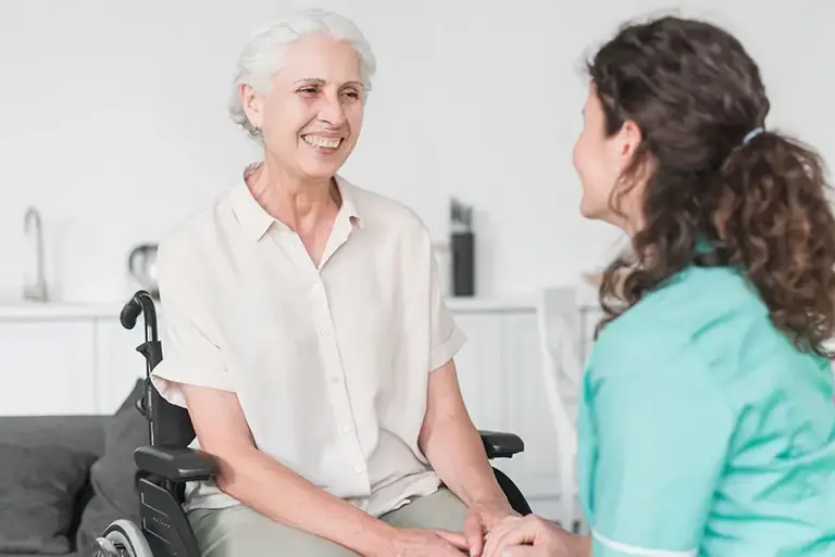 Healthcare professional holding hands with an older woman in a wheelchair