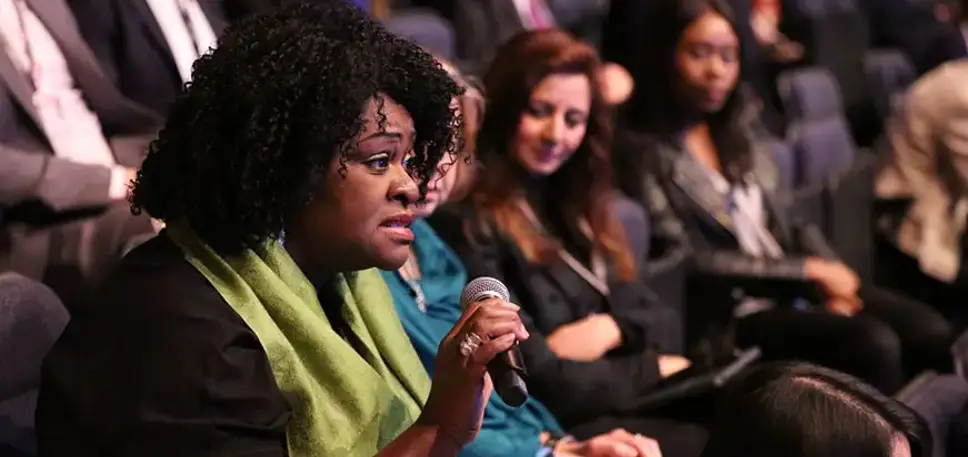 Woman in the audience of a large conference in a lecture hall stands with the microphone to ask her question