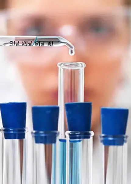 Close up of a rack of test tubes with a scientist adding a single drop from a pipette into the middle test tube.