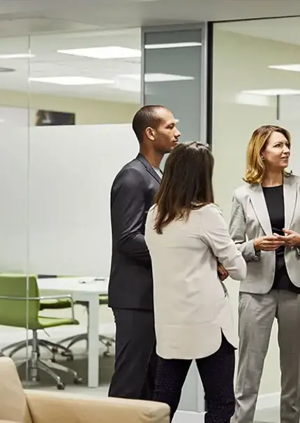 Four office workers stand talking in front of a set of glass meeting rooms