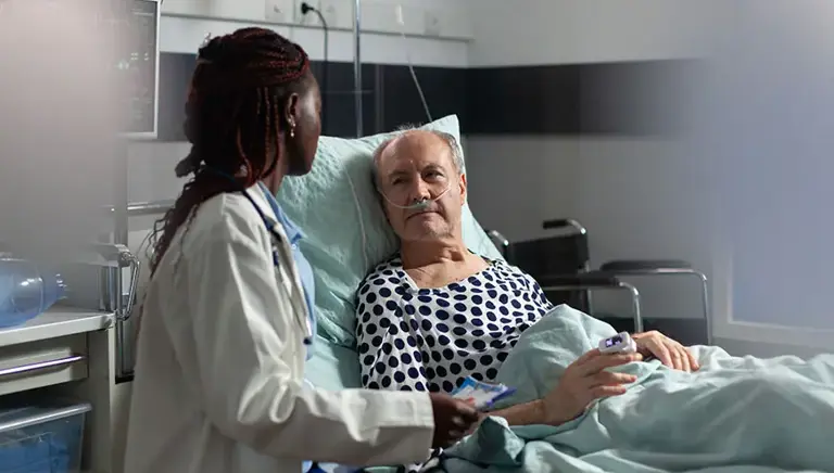 Doctor sits next to an older patient lying in a bed in a hospital setting