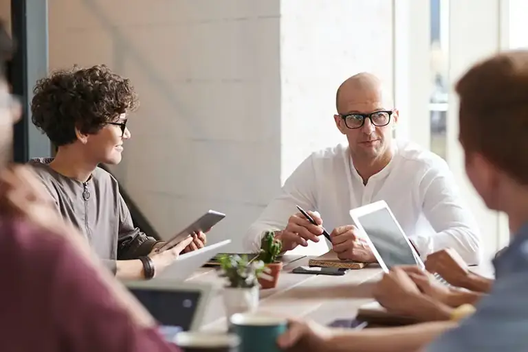 A team of casually dressed office workers sit a large desk having a meeting
