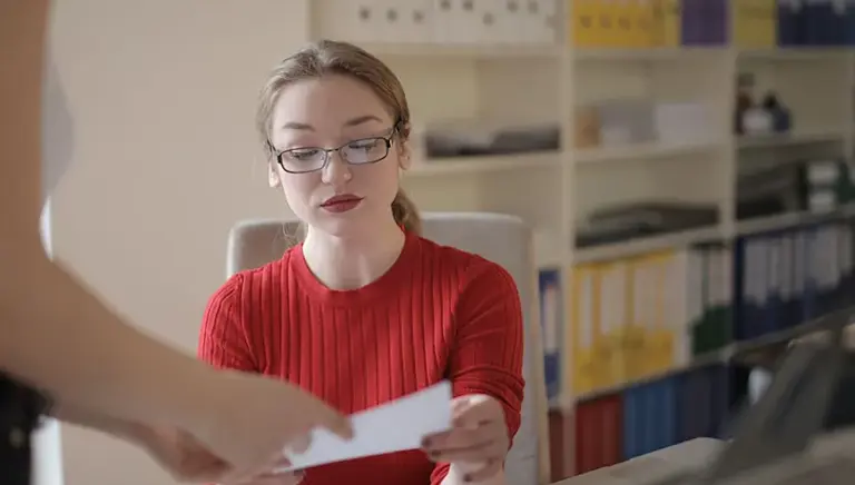 Seated office worker with library shelves of different coloured leverage arch files/records behind her