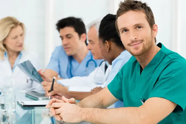 A line of five healthcare professionals in the background with the nearest facing us confidently