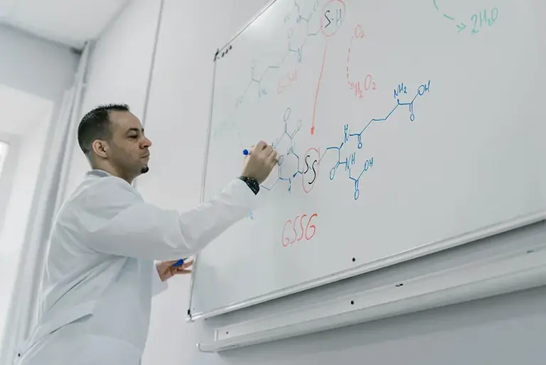 Scientist writes long molecular structures on a large wall mounted whiteboard 