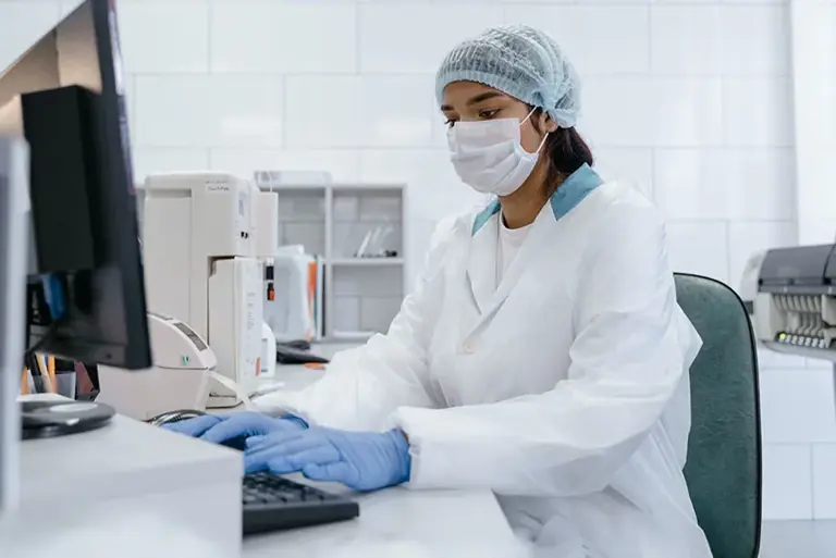 Masked scientist in a lab types on a computer