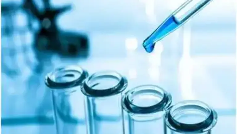 A drop from a pipette is about to be added to a set of test tubes in a lab